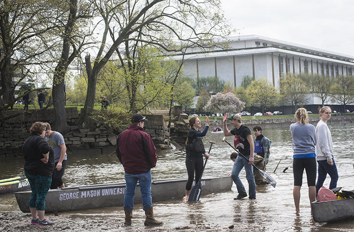 Group of students digging ground in lake and pushing a canoe.
